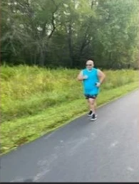 A person runs outdoors on a tree-lined path