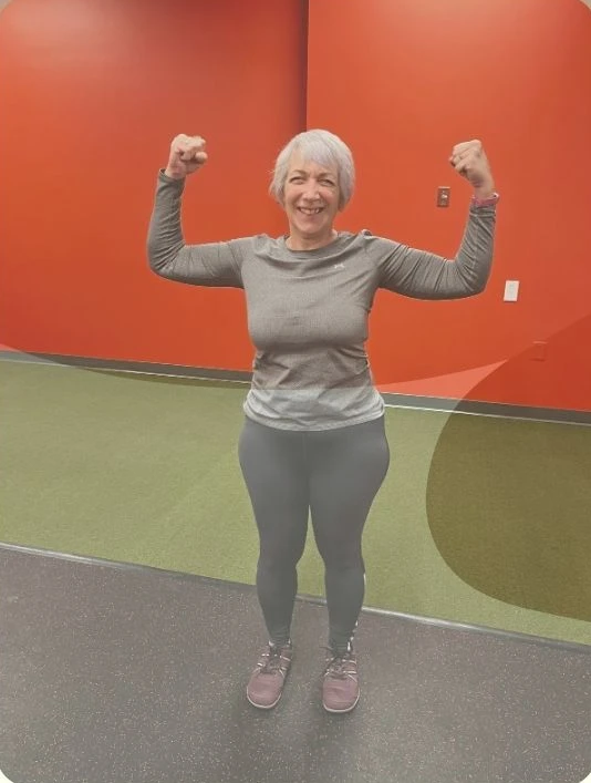 A smiling client flexes her arms in the gym