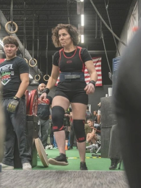 A lifter in a gym wearing a weightlifting belt and knee sleeves